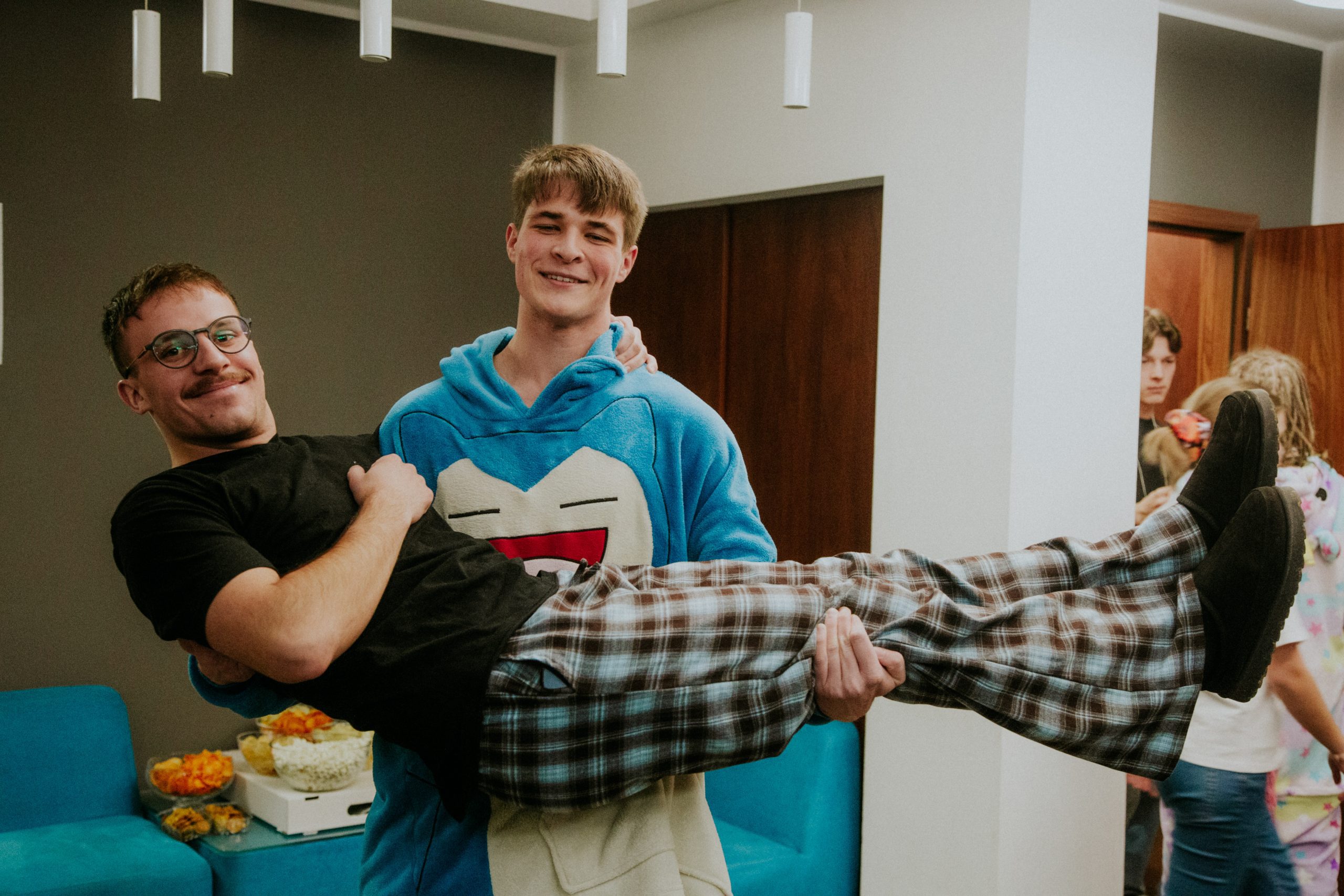 Zdjęcie przedstawia dwóch młodych mężczyzn. Jeden trzyma drugiego.